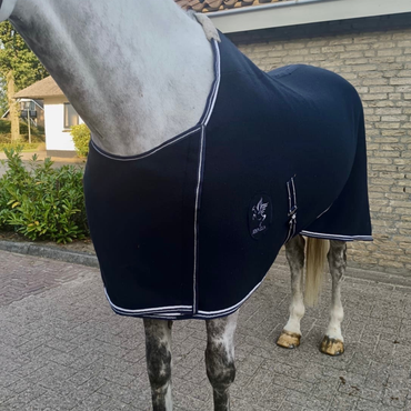 Horse wearing a navy blue saddle blanket with a logo on a pavement.