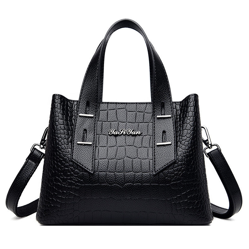 Black handbag with crocodile texture and visible brand name on a white background