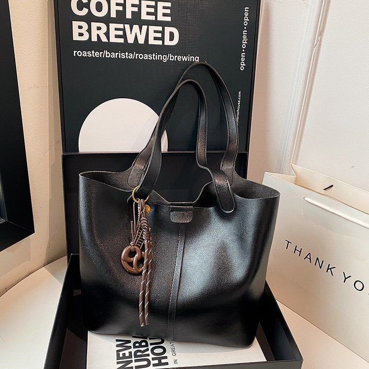 Black handbag with decorative charm on a white surface with a coffee-themed background