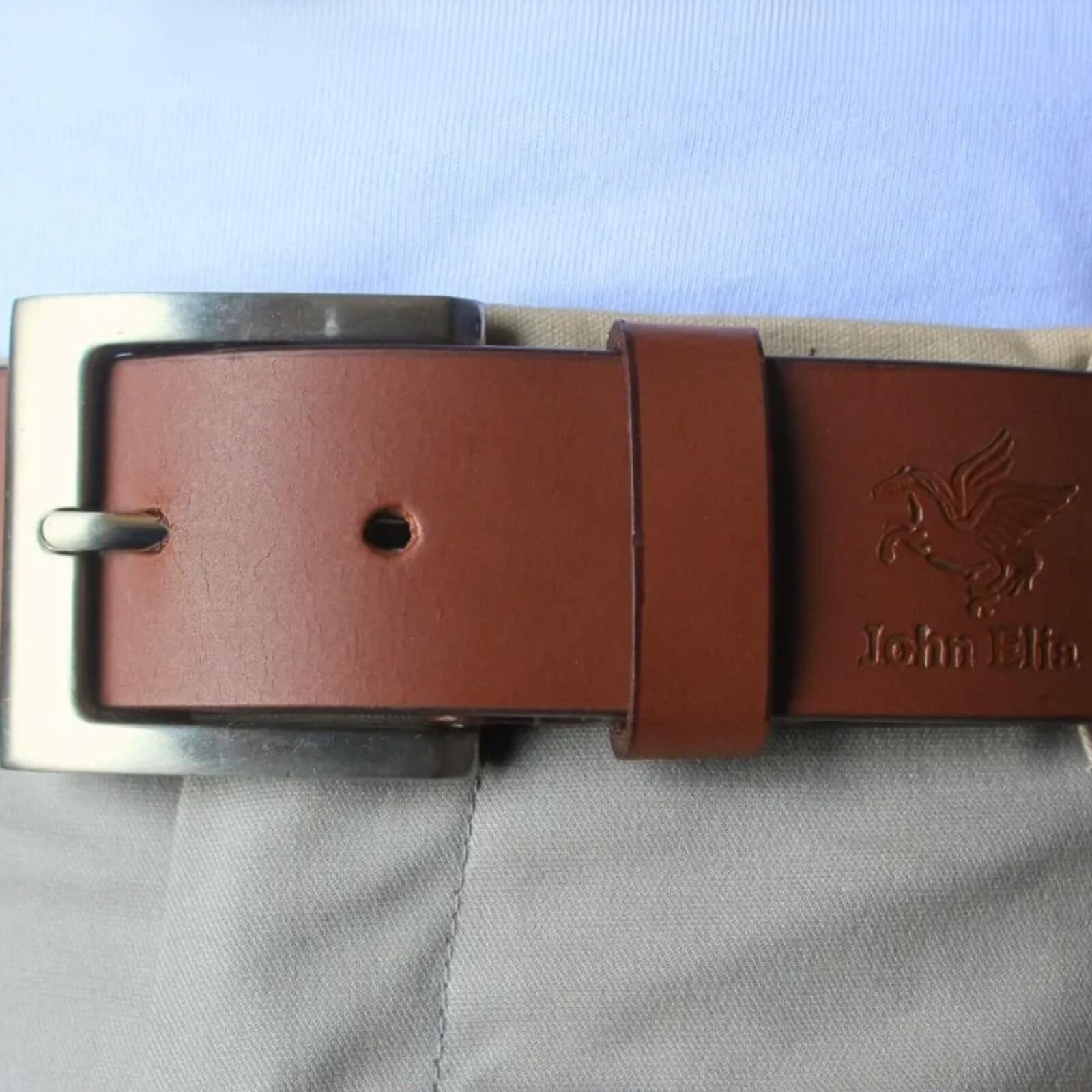 Brown leather belt with silver buckle on a light blue fabric background