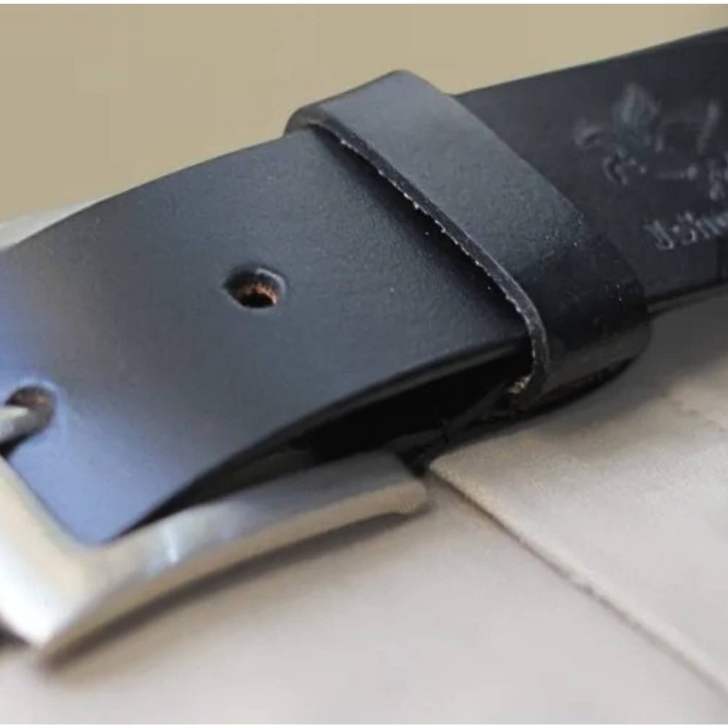 Close-up of a black leather belt with a silver buckle on a light surface.