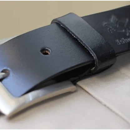 Close-up of a black leather belt with a silver buckle on a light surface.