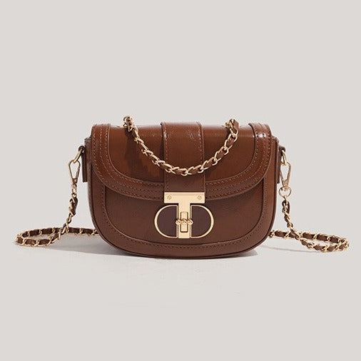 Brown leather handbag with gold chain strap on a light gray background