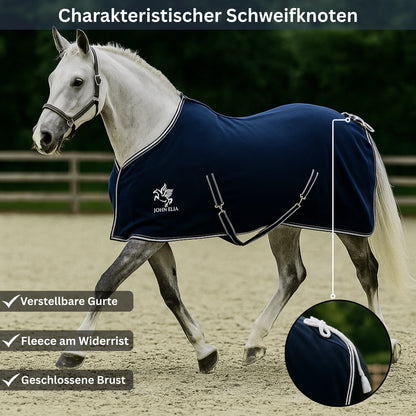 White horse wearing a navy blue rug with John Ella logo in an outdoor setting