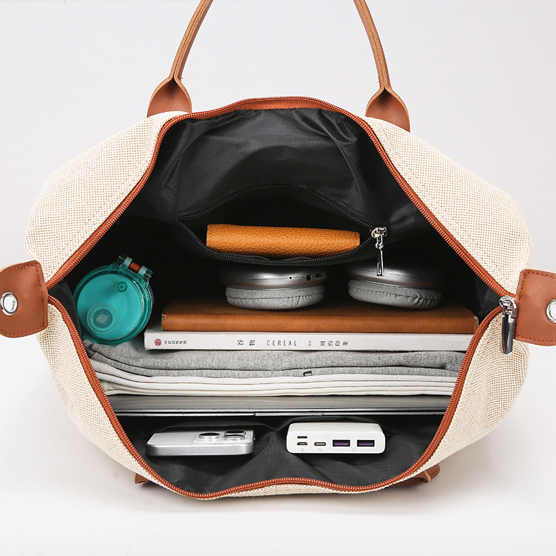 Open beige handbag with brown leather accents containing electronic devices on a light gray background