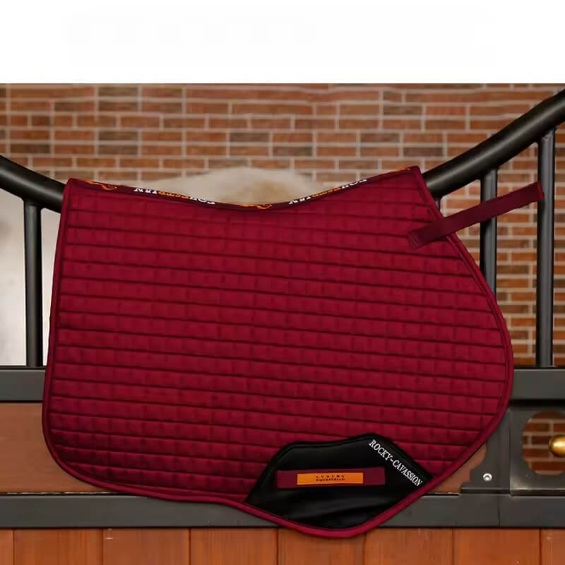 Red quilted saddle pad on a wooden surface with a brick wall background