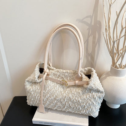 White textured handbag on a black surface with a white vase and books in the background.
